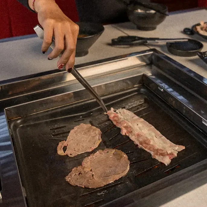 Premium wagyu beef grilling tableside at Raku Raku, the centerpiece of the comfort food menu