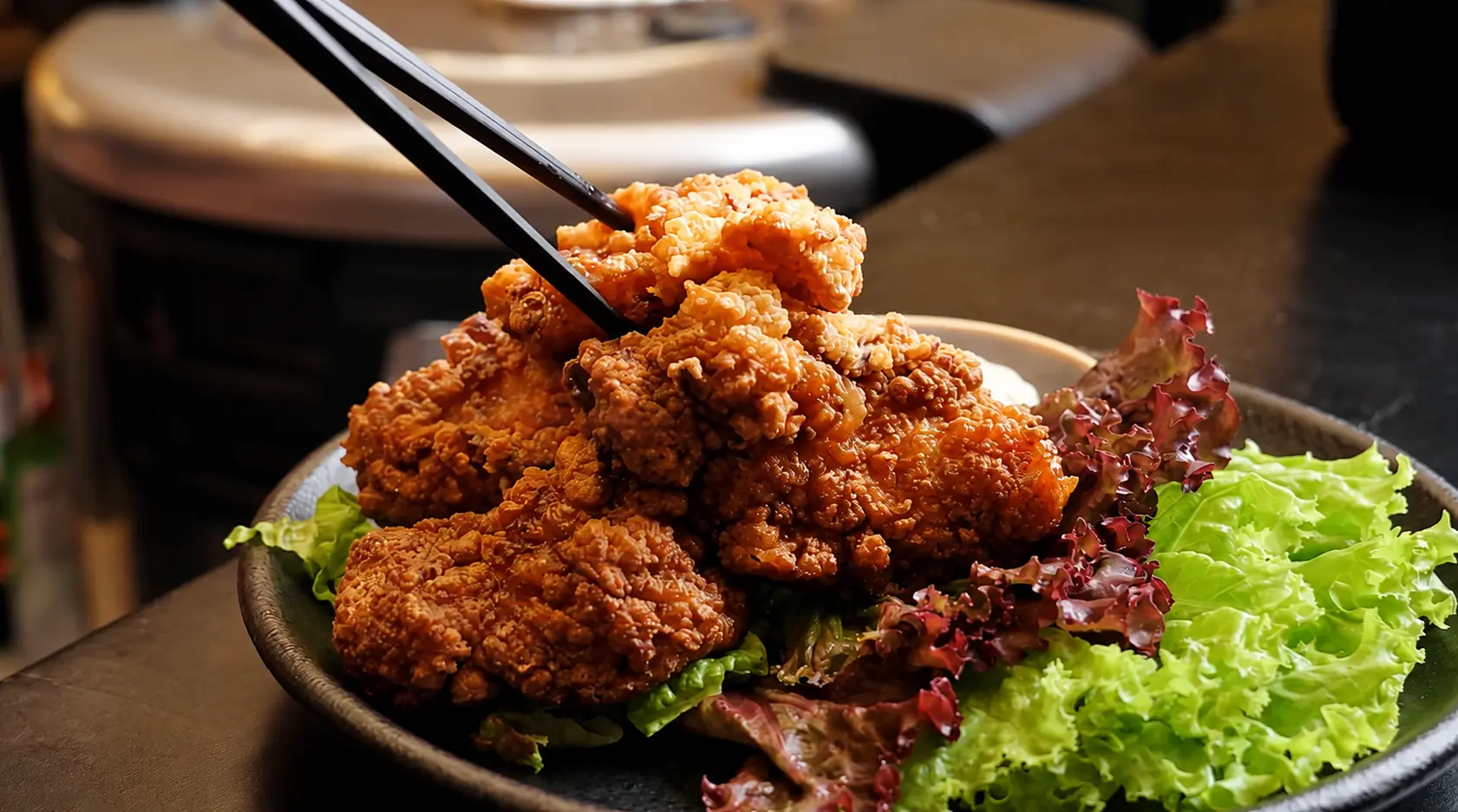 A plate of crispy chicken karaage served with fresh green and red lettuce, with chopsticks lifting a piece of the dish.